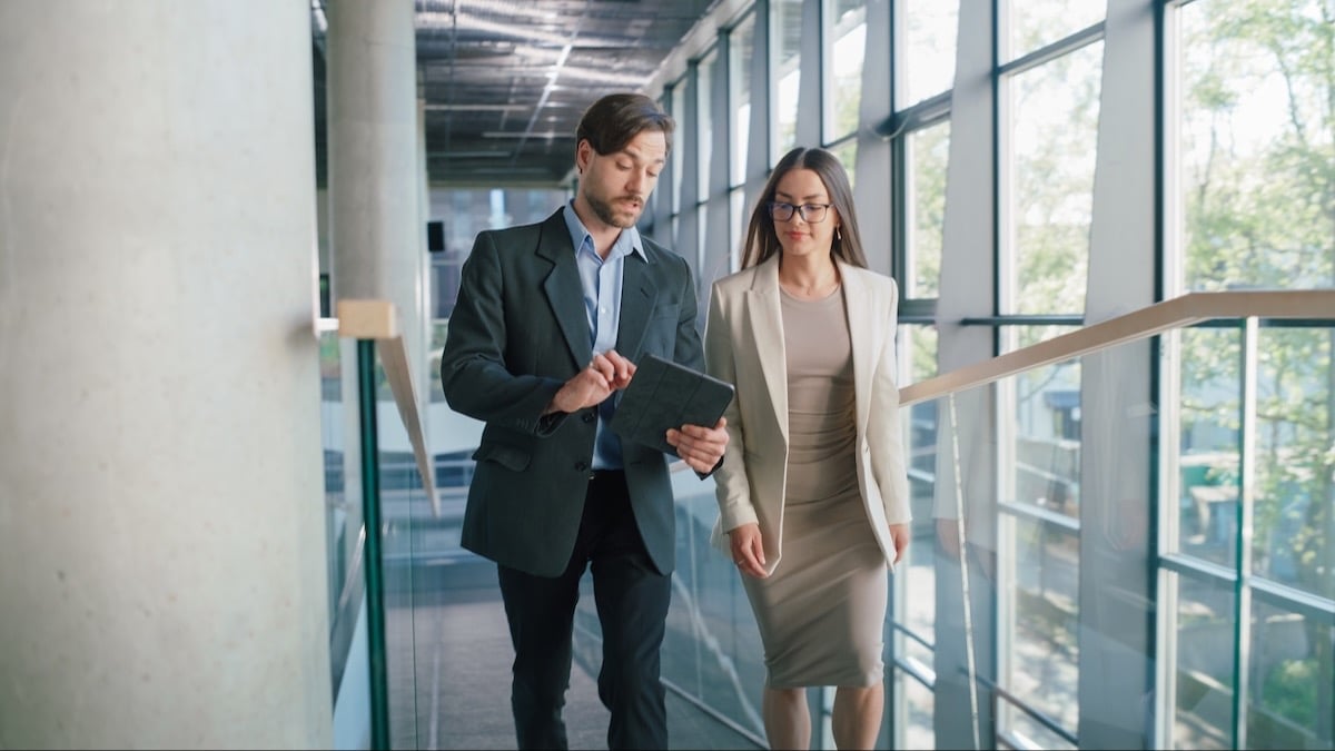 Two senior employees walk back to their department after a meeting, discussing where AI can improve a measurable business outcome first.