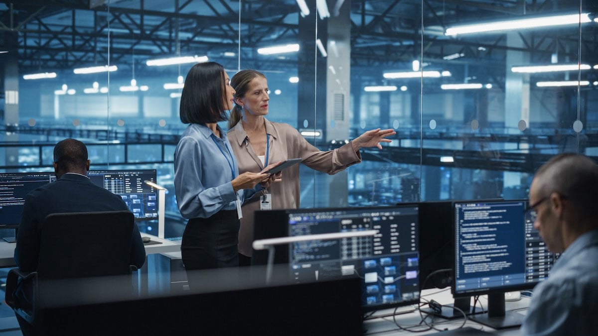Two senior leaders at a software company discuss projects over a tablet, showing how commitments made in everyday conversations drive company execution.