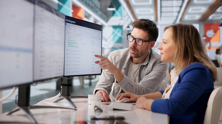 Two employees reviewing data on a desktop monitor, highlighting the importance of trusted data, governance, and readiness before deploying AI across the organization.