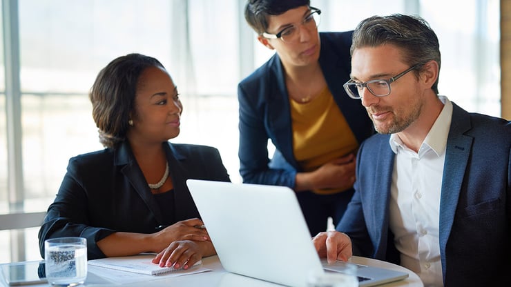 Three professionals review information on a laptop together, representing how private equity leaders evaluate AI governance, risk, and diligence readiness across portfolio companies.
