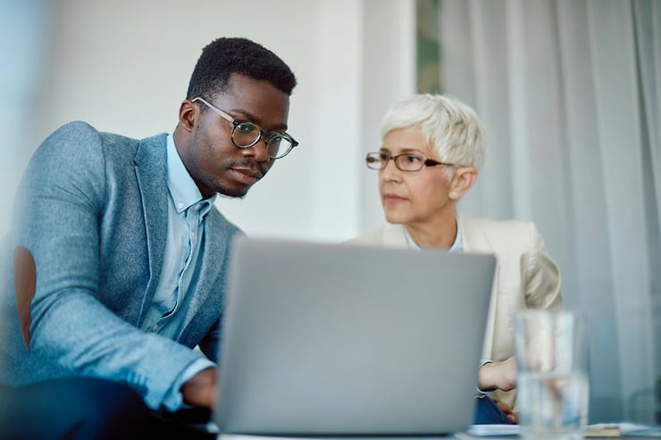 The two employees analyze the Purview dashboard to review compliance scores and active risks, helping them quickly prioritize and address key issues in their organization's data estate.