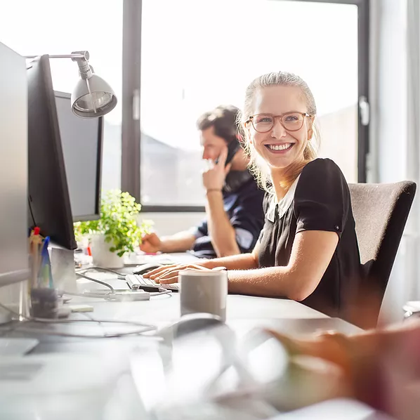 A female employee sits at her work desktop in the office, smiling as she types away, impressed by Microsoft 365's seamless integration of cloud applications that unlock endless opportunities for creativity and productivity, empowering her to accomplish more with ease.