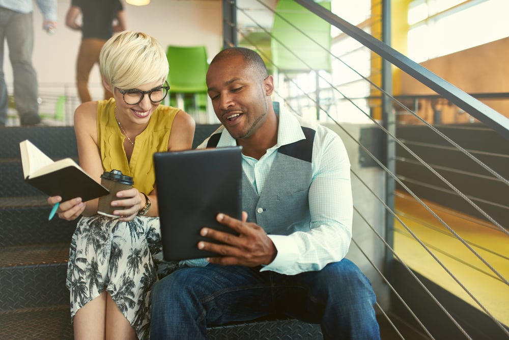 Two small business owners working on business strategy using a digital tablet while sitting in staircase