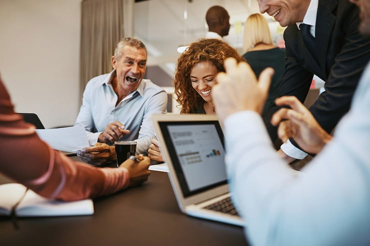 A group of IT directors at an accounting firm gathers in a conference room, discussing their transition from an Enterprise Agreement to Microsoft CSP while reviewing Synergy’s licensing strategy on a shared laptop—smiling as they realize the new model offers the flexibility and clarity they need to scale efficiently and support future growth.