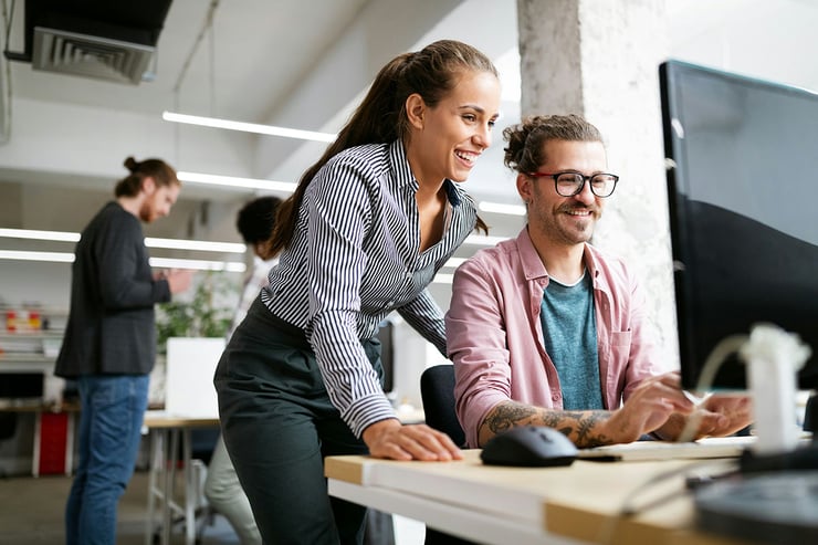 Two employees excitedly explore AI capabilities on a laptop in a modern office setting.