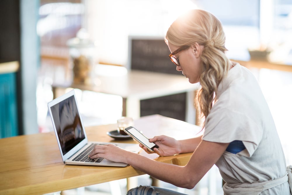 Woman using a laptop and mobile phone in cafx92xA9