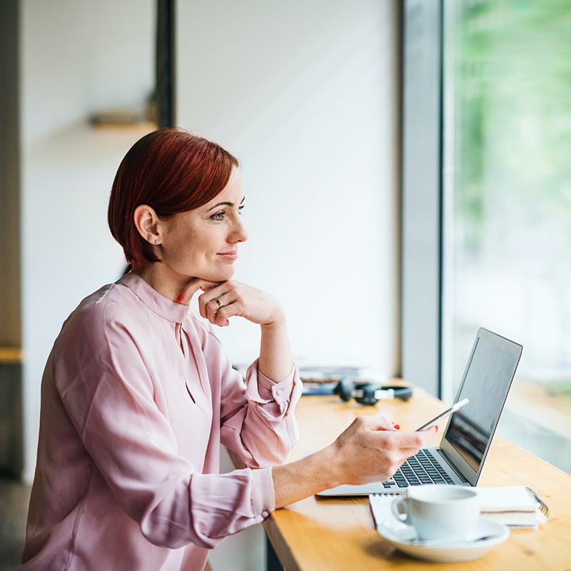 Picture of employee working remotely in a cafe & typing prompts into Microsoft Copilot in Word to jump-start the creative process for her upcoming presentation.