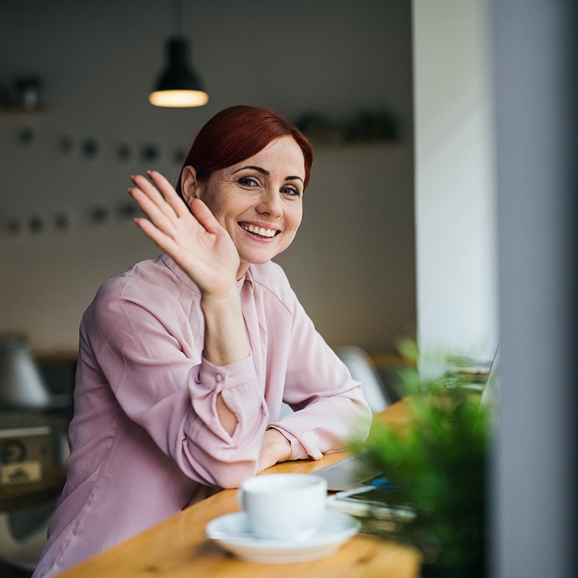 Picture of employee working remotely in a cafe & turning her existing Word document that she crafted & transforming that into a PowerPoint presentation using Microsoft Copilot.