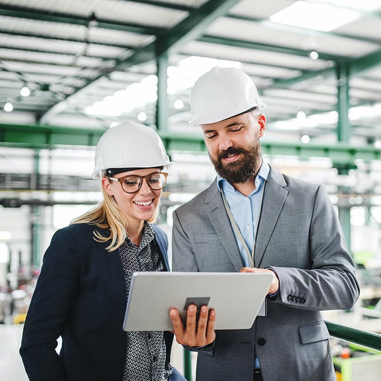 Picture of employee showing another employee the capabilities offered to them by Microsoft Copilot in Excel to help them analyze & explore the data for the efficiency of their assembly line in their manufacturing plant so they can make continuous improvements.