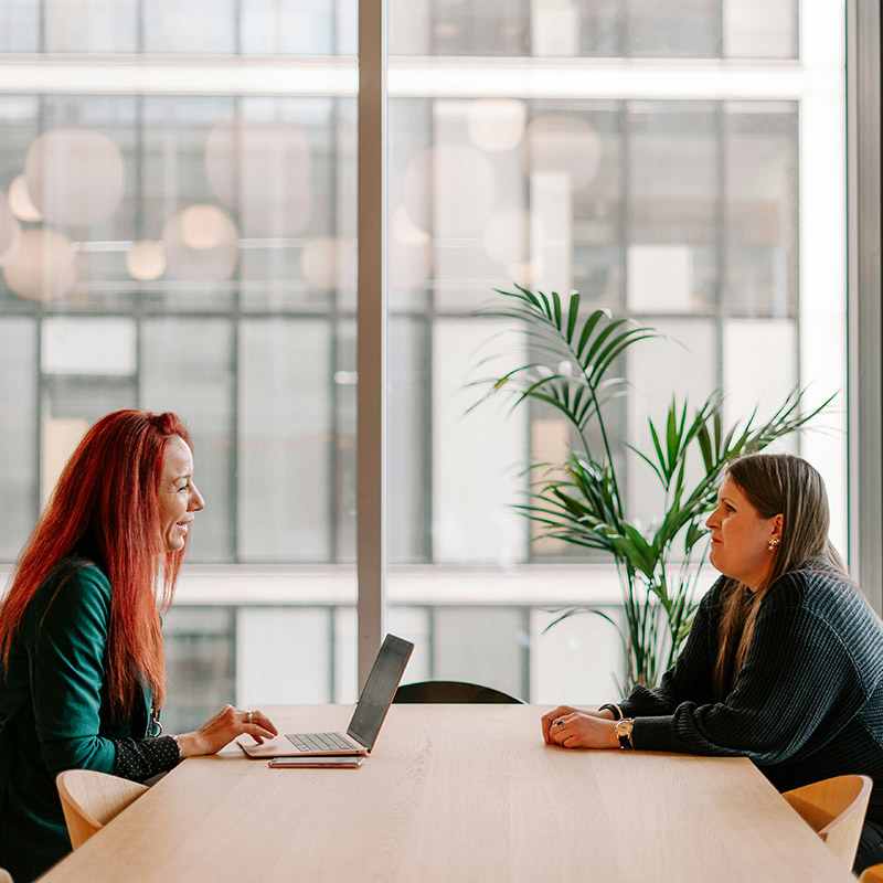 Two female employees meet to discuss a project in Microsoft 365, trusting that tools like Purview Audit provide behind-the-scenes accountability across their environment.