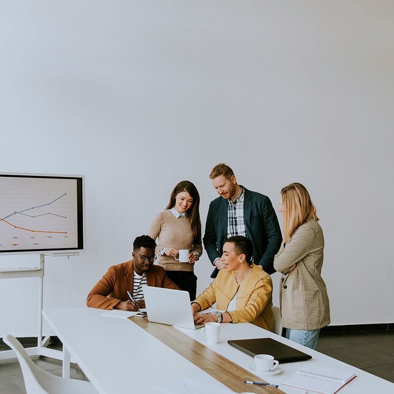 Colleagues crowd around a laptop and use Word’s Apply Sensitivity button; Purview DLP binds the label to the document so every future email or upload respects its protection level.