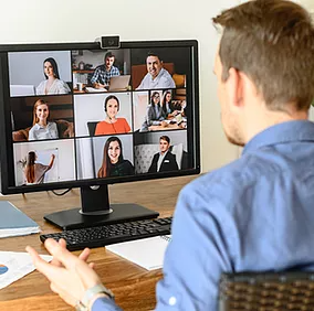 A male employee sits at his home desk, taking a Microsoft Teams call with his marketing team to discuss an upcoming campaign, seamlessly sharing, saving, and accessing files through Microsoft OneDrive to ensure smooth collaboration and progress.