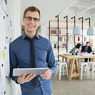 A male employee smiles while holding his tablet, browsing Microsoft Stream to watch company-shared videos, training sessions, and updates, staying engaged and informed from anywhere.