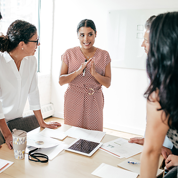 In an engineering firm’s meeting room, four female engineers stand exchanging ideas, while one team member uses Microsoft Teams to document discussions, share files, and edit content in real time for seamless collaboration.
