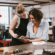 Two female employees at an architecture firm use a tablet with Microsoft Teams to access team-shared files, including architecture sketches, documents, and other project materials, ensuring seamless collaboration and real-time updates.