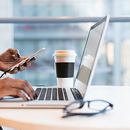 An employee accesses her synced emails and calendars across all devices, holding her work mobile device in one hand while typing on her laptop, ensuring seamless connectivity and organization anytime.